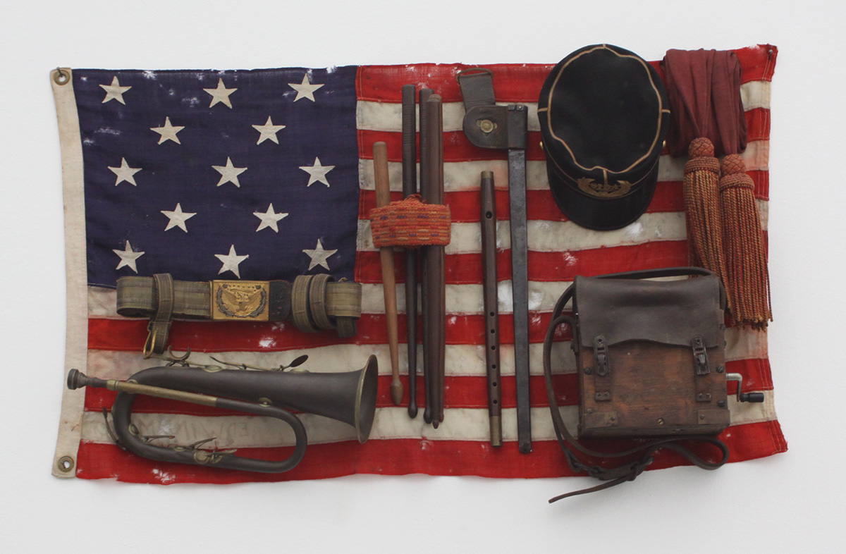 Danh Vo, She was more like a beauty queen from a movie scene, 2009, Brass bugle, felt cap with velvet, bayonet sheath, field radio with wood and leather case, sashes, wooden drumsticks, fife, leather sword belt with gold and silver details, and 13-star American flag, 54.5 x 96.5 x 13.5 cm, © Danh Vo, Photo: Jean-Daniel Pellen-Paris, Collection Chantal Crousel