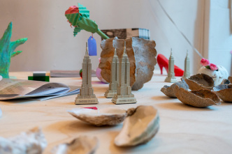 hanzhai Lyric. Canal Street Research Association in retail drag. 2020. A history of the area is mapped out in found objects. Pictured here are “Lady Liberty” by Betty Roytburd, a paper rose by Nothing Man, oyster-inspired ceramics by Ruby Chang alongside oyster shell candles, skyscraper souveniers and bootleg perfumes in the form of stilettos walking through the landscape. Image courtesy the artists. Photo: Parker Menzimer