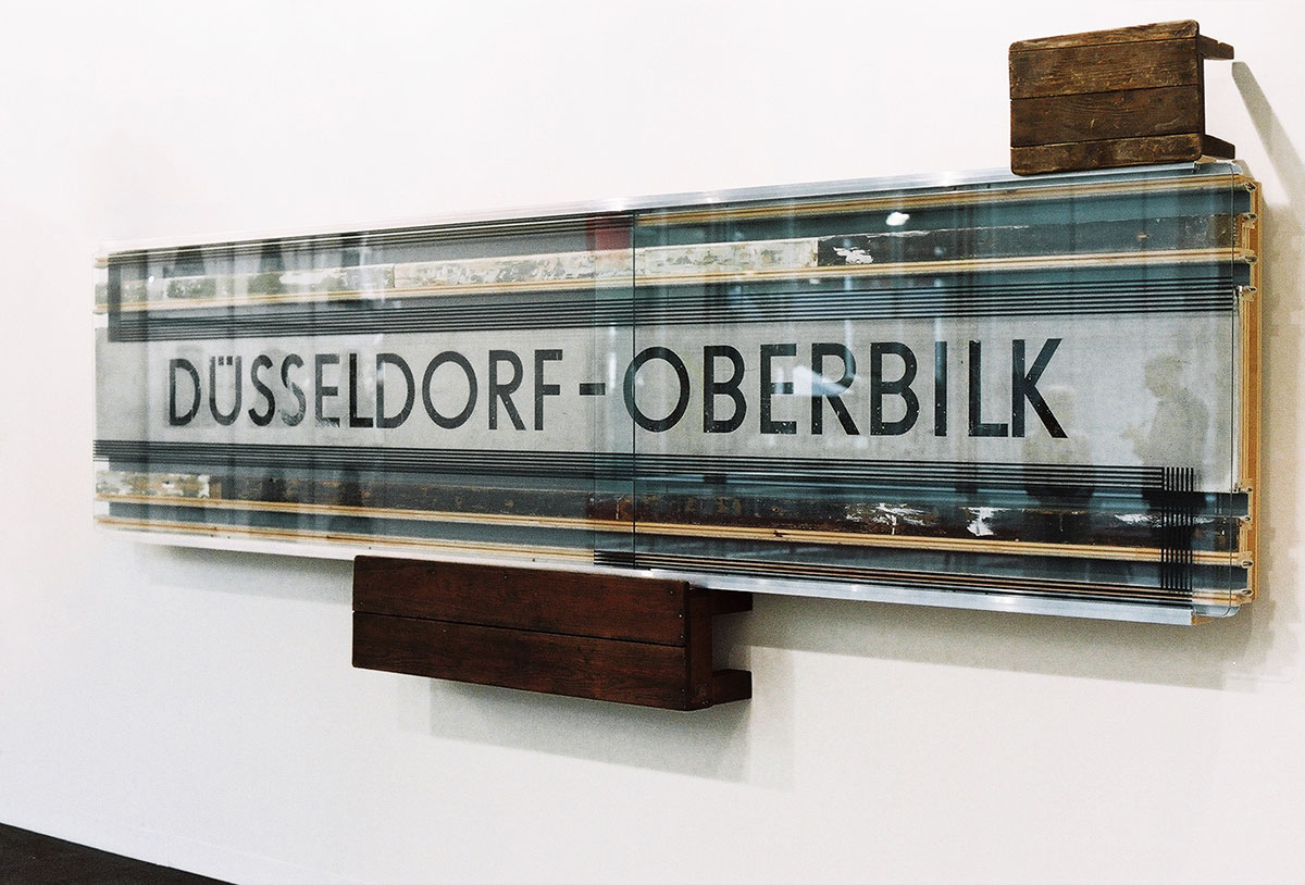 Reinhard Mucha, Das Haus auf seinen Schultern, Für Dieter Forte, 2013, 2 footstools, solid wood (found items), aluminum profiles, alkyd resin paints painted on the reverse side of float glass, station sign alkyd resin paints, aluminum sheet (found item), baseboards in various paint colors and synthetic resin spatula, solid wood (found items), felt, plywood, blockboard, 144.8 × 373.8 × 25.4 cm, Collection Michael Ballack, © muchaArchive / VG Bild-Kunst, Bonn 2022
