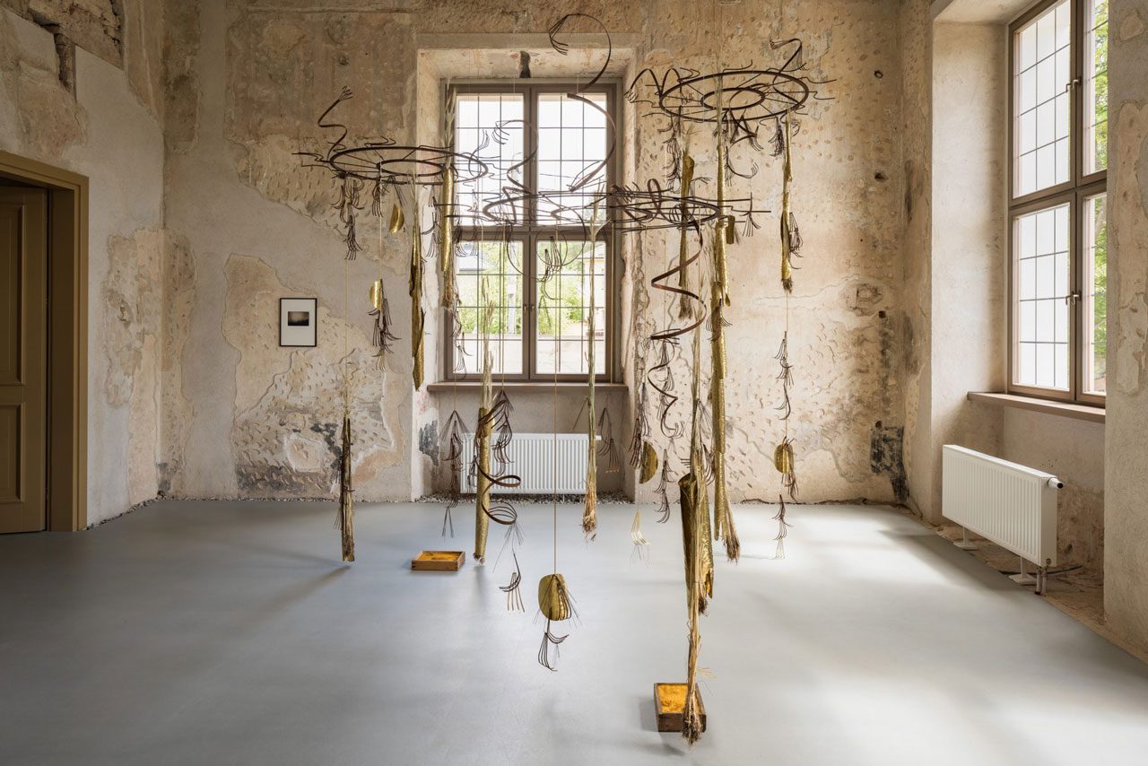 za Tarasewicz. Looped Processions IV, 2022. Oxidised steel, brass, wheat, wire in three segments. Dimensions variable; and Yellow Coal, 2016/2022. Ochre, wood. Dimensions variable.
