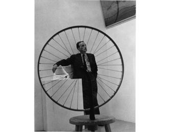 Marcel Duchamp inside the exhibition "The Art of Assemblage" at the Museum of Modern Art, New York, 1961, with his artworks "Fountain" (1950, replica of lost 1917 original) and "Bicycle Wheel" (1951, replica of lost 1913 original), Artwork: © Association Marcel Duchamp/ADAGP, Paris/Artists Rights Society (ARS), New York 2026, Photo: Marvin Lazarus